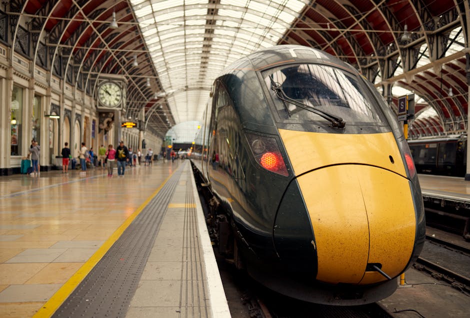 Inside Paddington Station at dusk, the platform area features a high, arched metal and glass ceiling illuminated by overhead lighting. On the left side, there is an ornate clock mounted on a decorativ